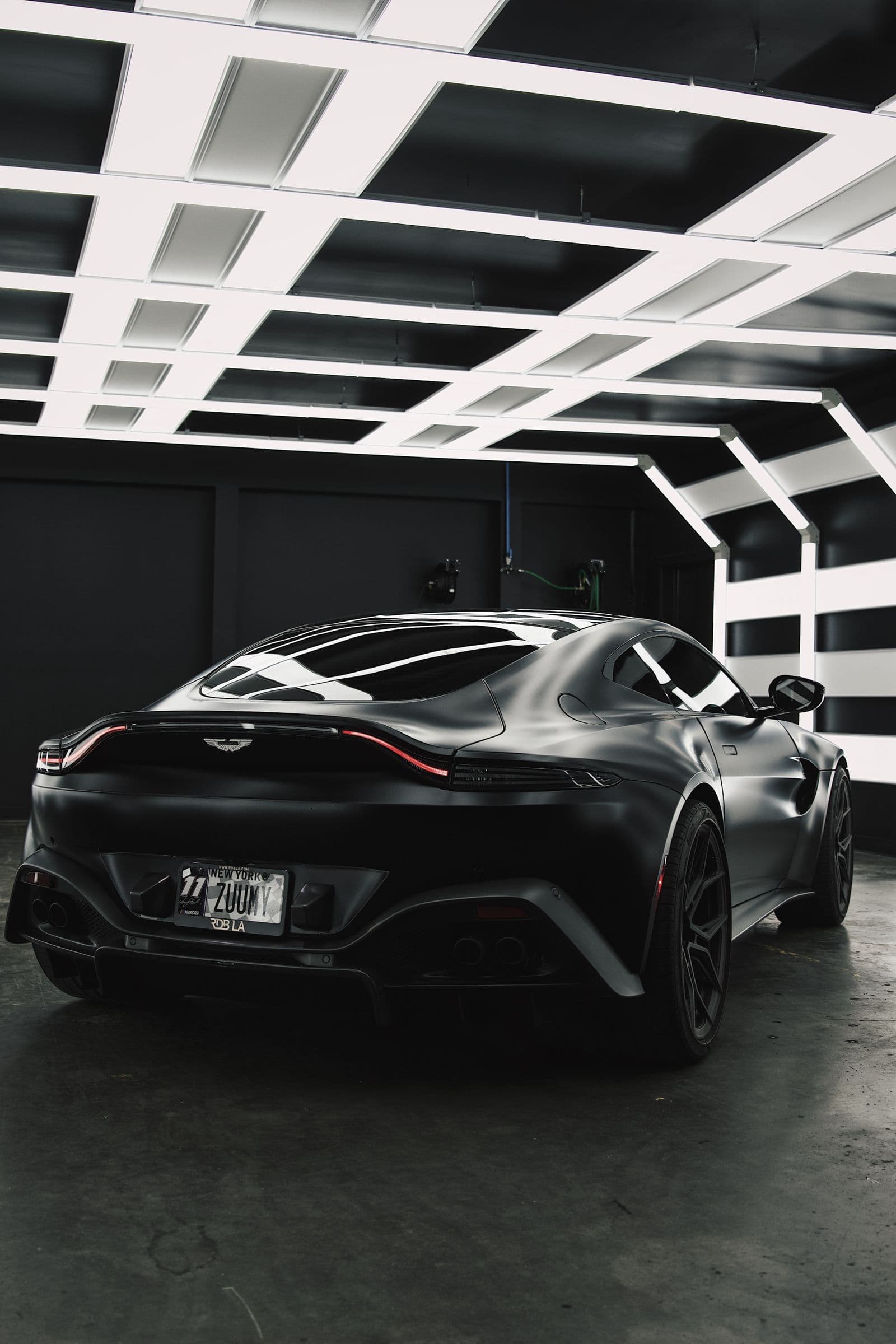 Collector car beneath a geometric light ceiling over a dark reflective floor — metallic design territory
